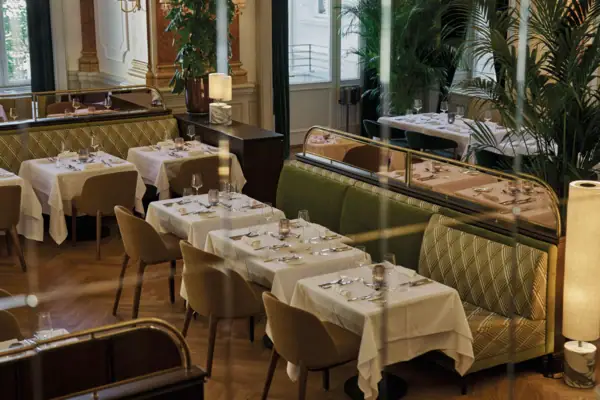 A restaurant interior with neatly arranged tables and chairs, featuring window views and elegant table settings.