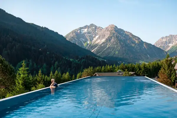Eine Frau sitzt am Pool mit Bergen im Hintergrund.
