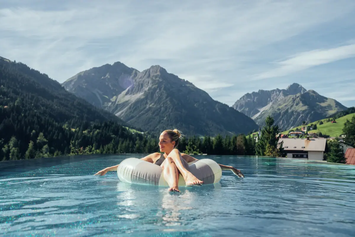 Swimming pool at the A-ROSA Ifen Hotel Kleinwalsertal A woman is floating on a rubber ring in a swimming pool, with mountains in the background.