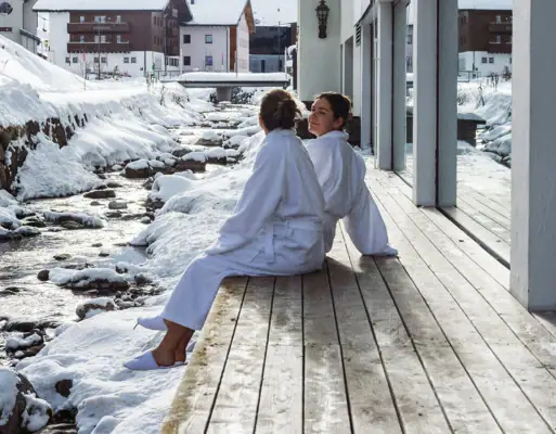 Two women are sitting on a veranda in front of a building outdoors.