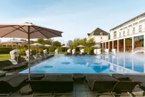 Großes weißes Gebäude mit Pool und Bäumen im Vordergrund.