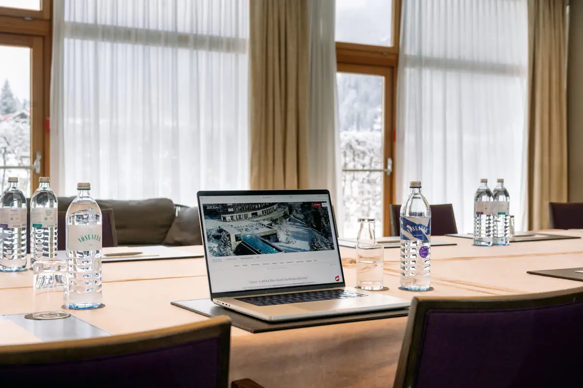 Ein Laptop steht auf einem Tisch in einem Tagungsraum mit Wasserflaschen und einem Fenster im Hintergrund.