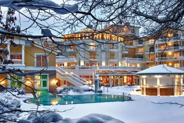 Building with a pool in the middle of a mountain village, surrounded by trees and a landscape with mountains.