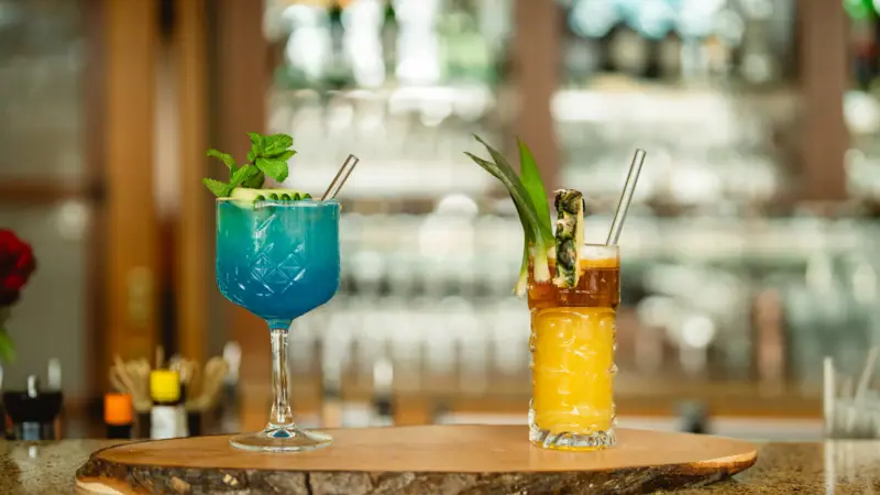 Two glasses containing different coloured drinks on a bar.