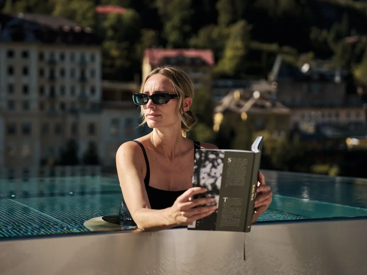Woman relaxing with a book in the rooftop infinity pool at the Straubinger Grand Hotel in Bad Gastein with panoramic mountain views.