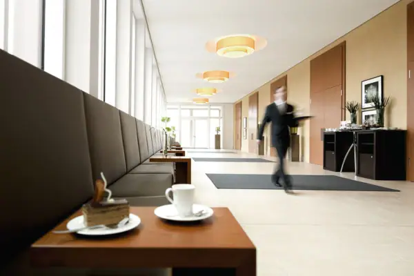 Ein Mann geht in einem Flur und im Vordergrund ist ein kleiner Tisch mit einem Stück Kuchen und einer Tasse zu sehen.