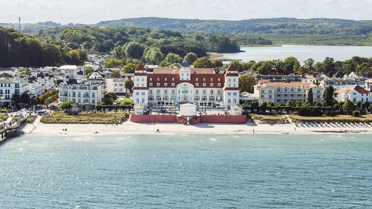 A-ROSA Kurhaus Binz A large white building next to a lake under a cloudy sky.
