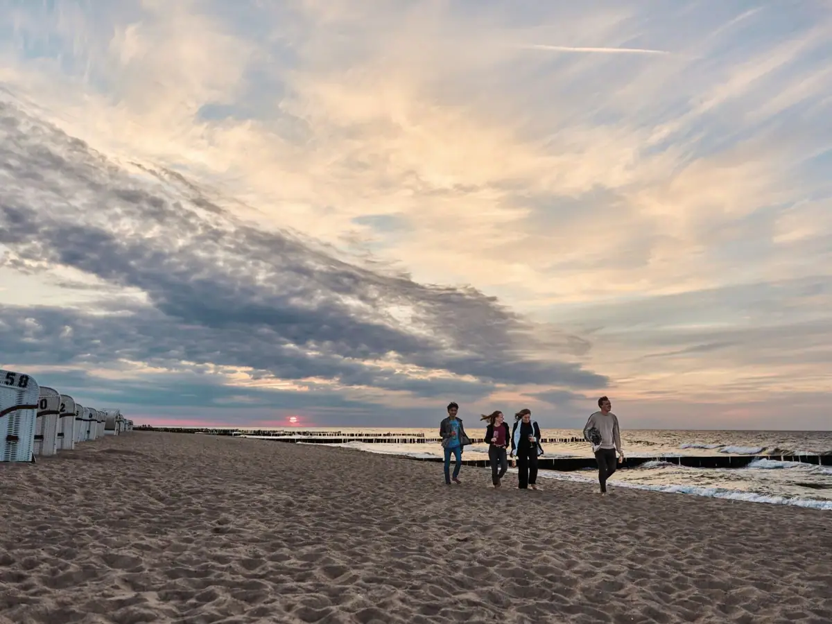 A group of people walking along a beach under a partly cloudy sky.