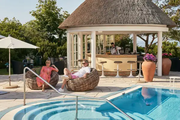 A man and woman sitting in wicker chairs next to a swimming pool at a resort.