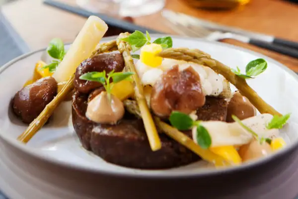 Ein Teller mit einem raffieniert angerichtetem Gericht, dahinter ist eine Gabel und ein Messer zu sehen.