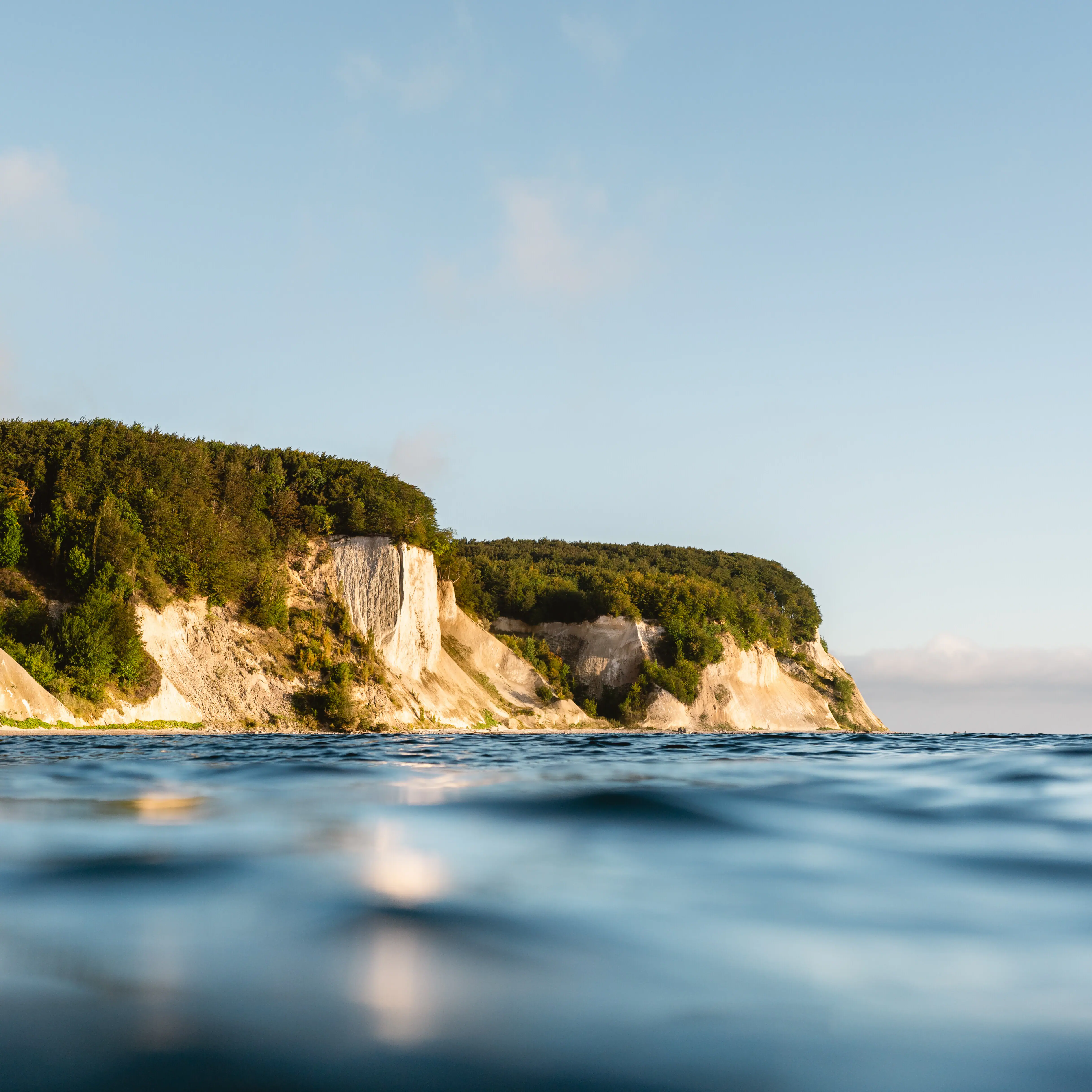 Water with a cliff and trees under a partly cloudy sky.