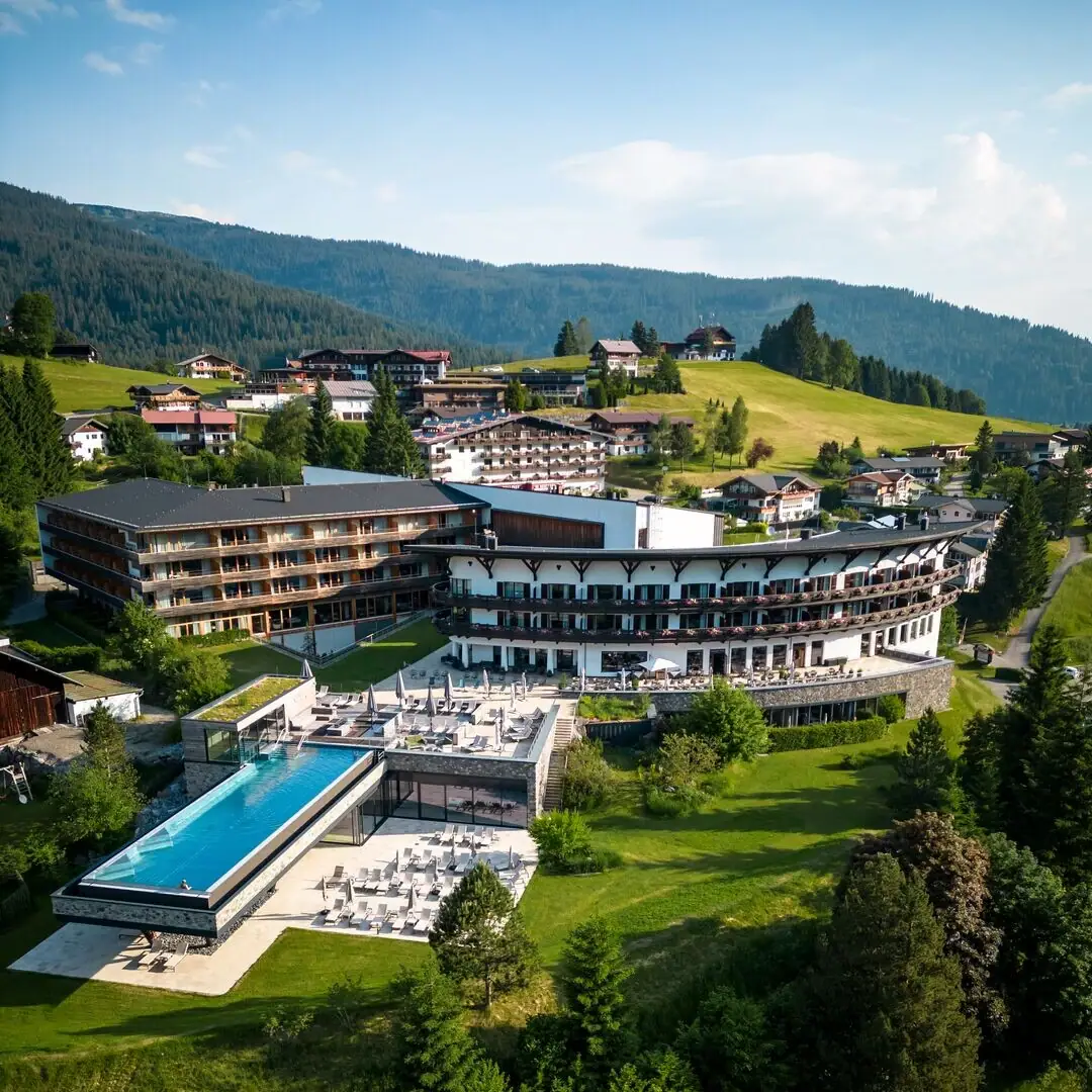 Ein Gebäude mit einem Infinity Pool inmitten eines Bergdorfs, umgeben von Bäumen und Grünflächen.