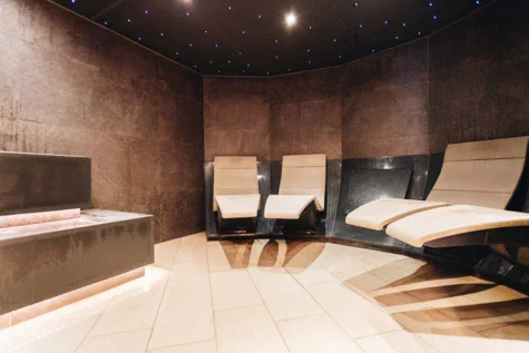 A mineral steam bath with stone walls and floor. Seats are attached to the walls and little blue lights are shining on the ceiling like a night sky. 