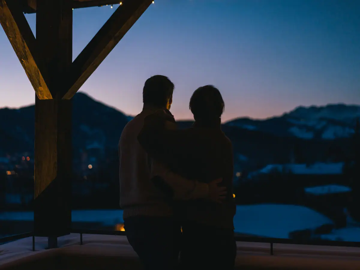 Two people hugging in front of a mountain.