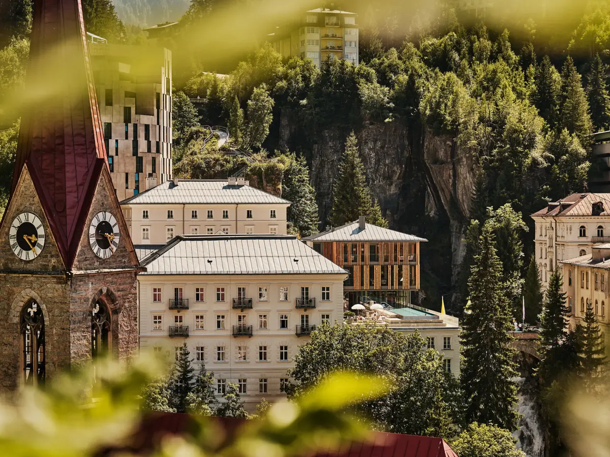 View of Straubinger Grand Hotel and church tower at Straubingerplatz in Bad Gastein, Salzburger Land, surrounded by mountains.