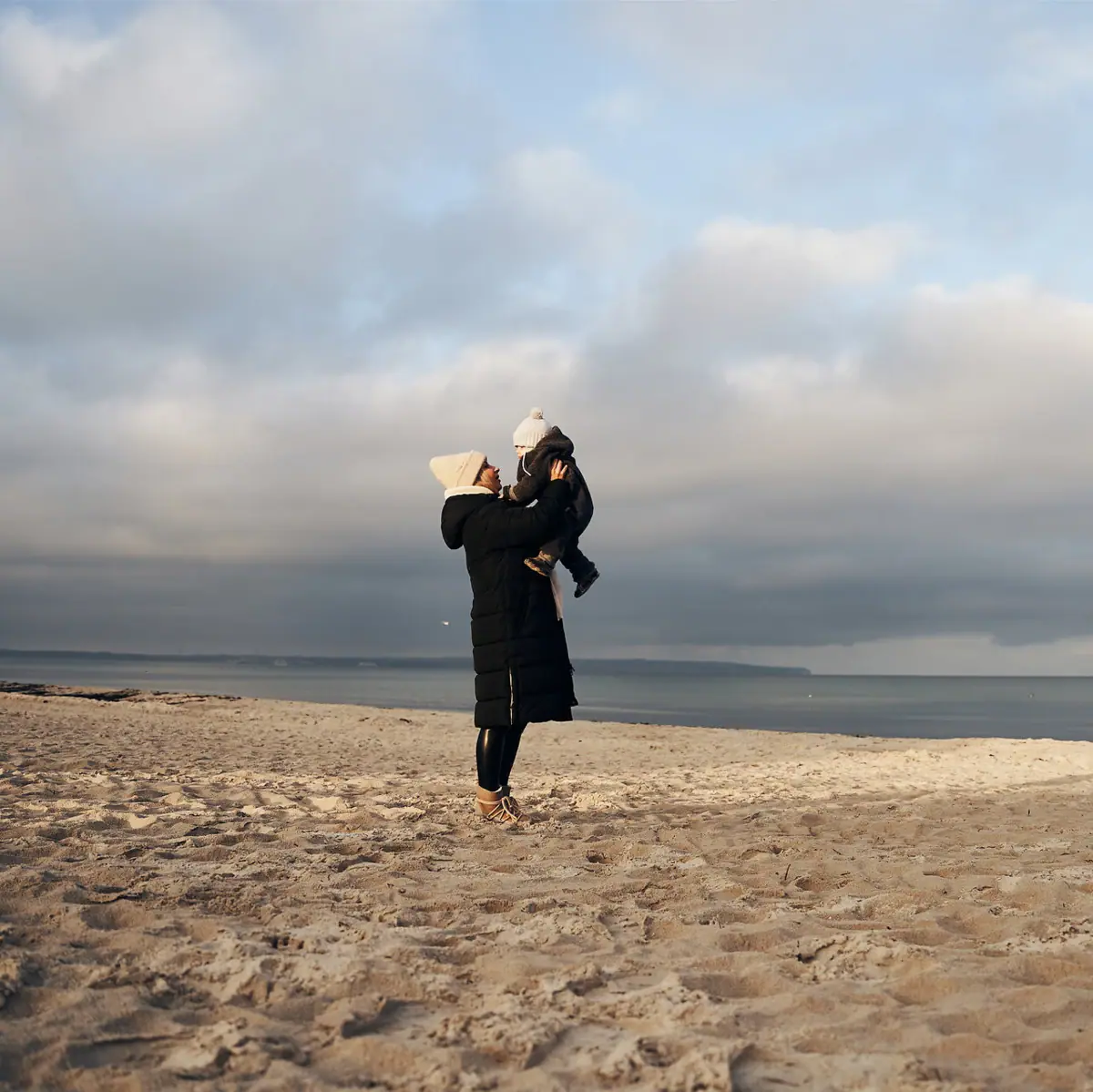 A woman is holding a baby on the beach.