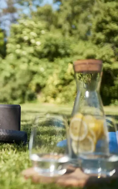 On a green meadow stands a carafe of lemon water with glasses next to it. 