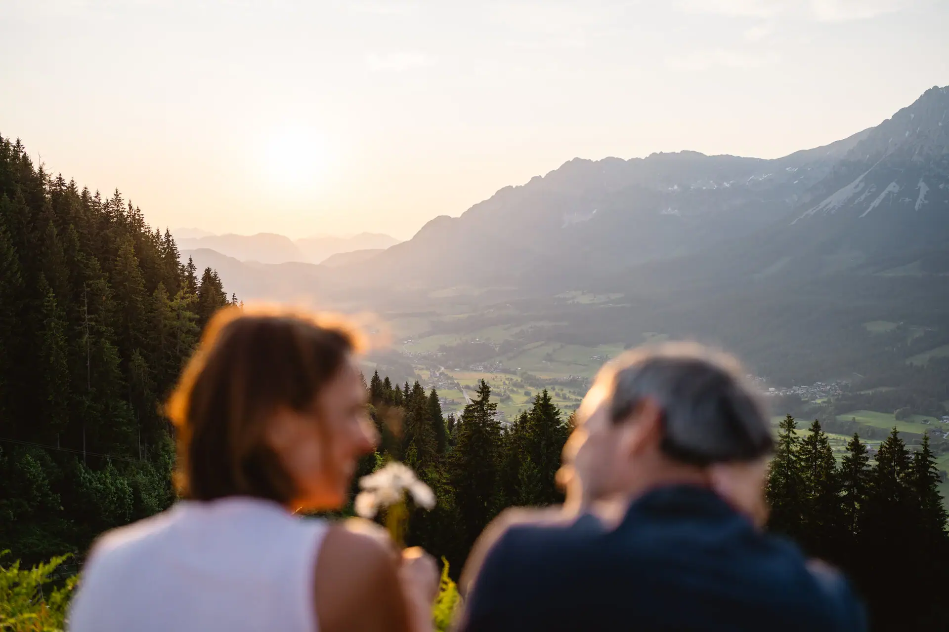Ein Mann und eine Frau sitzen auf einem Hügel mit Blick auf ein Tal.
