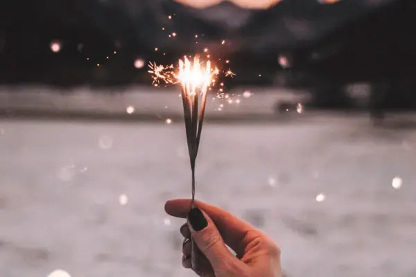 Hand holding a lit sparkler against a sky background.