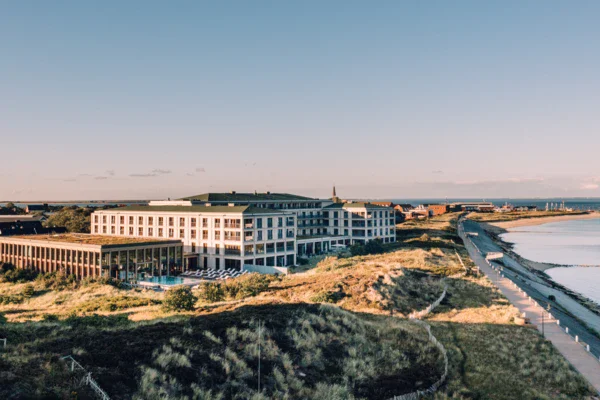 An aerial view of the A-ROSA Sylt, which is surrounded by dunes and close to the water, at dawn.