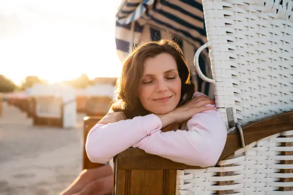 A woman smiling while leaning on a chair outdoors.