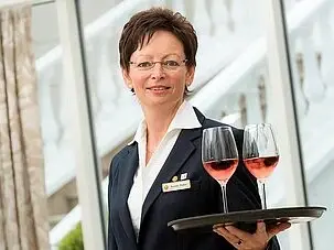 Woman in suit holds tray with wine glasses and smiles.