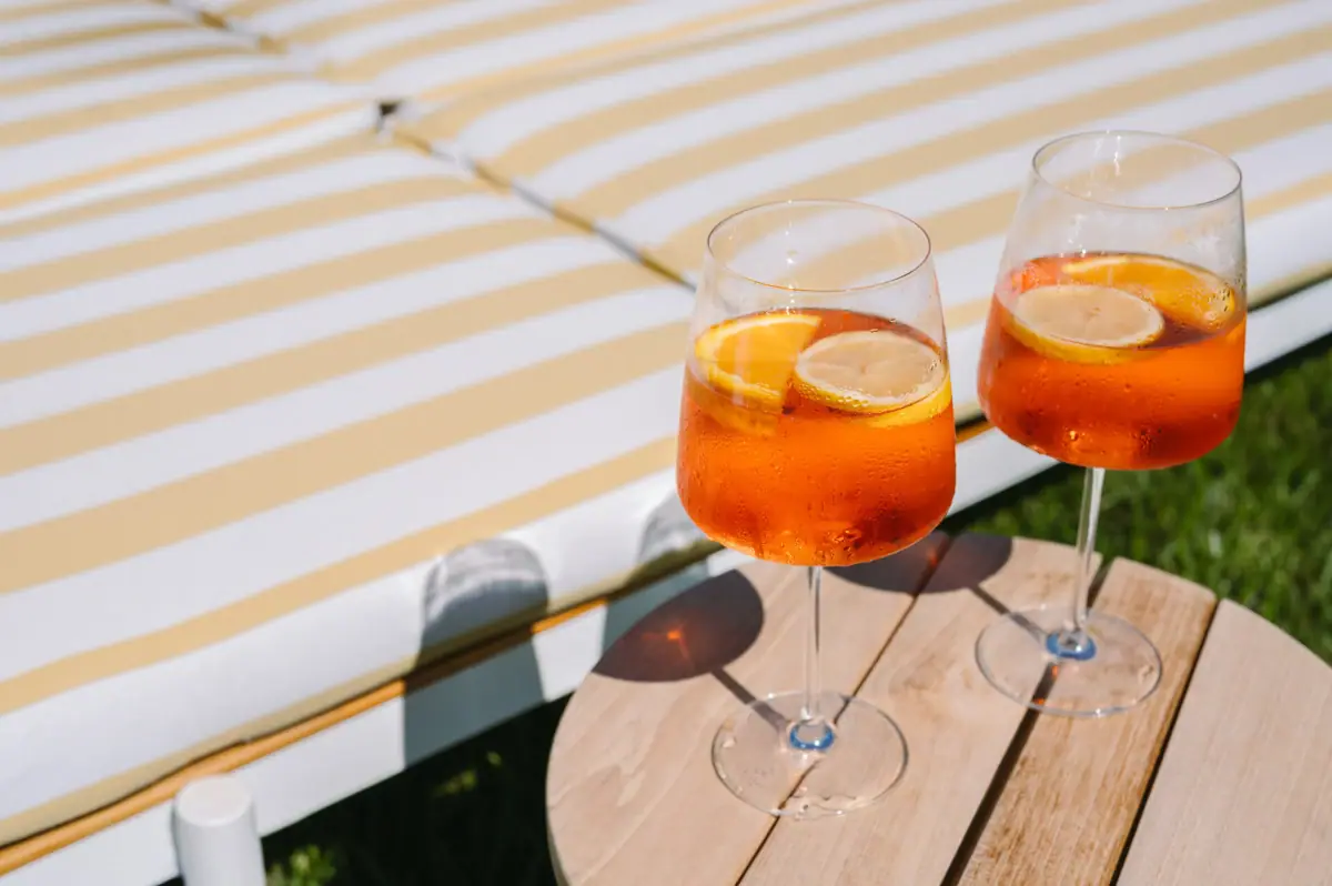 Aperol Spritz Two glasses containing an orange-coloured liquid and slices of lemon on a table.