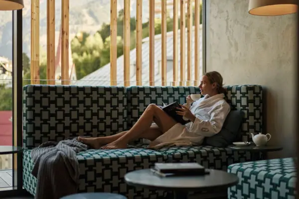 Woman in bathrobe reading with mountain views at Straubinger Grand Hotel Bad Gastein.