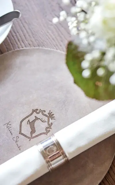 Napkin with ring on a beige placemat with the inscription "Kilian Stuba" on a wooden table.