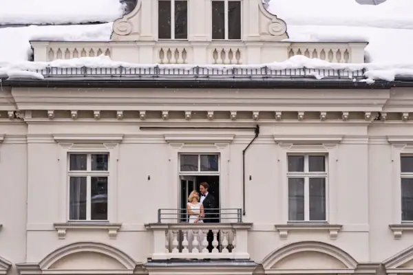 A man and woman standing on a balcony in front of a building facade.