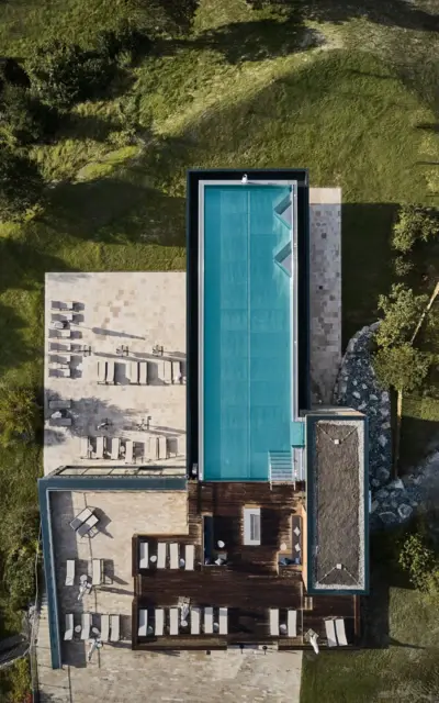 Swimming pool with sun loungers on a terrace, surrounded by grass and plants from a bird's eye view.