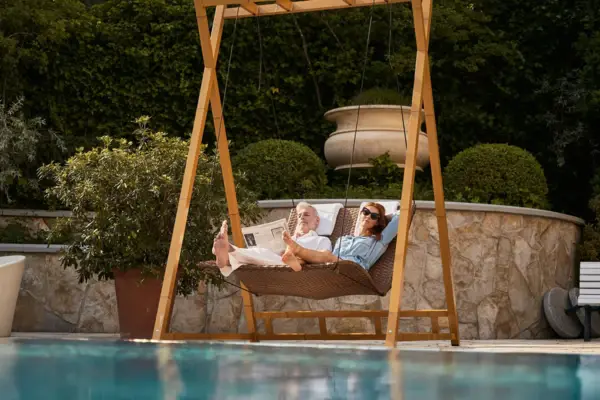 A man and a woman are lying on a swing, surrounded by plants and trees.