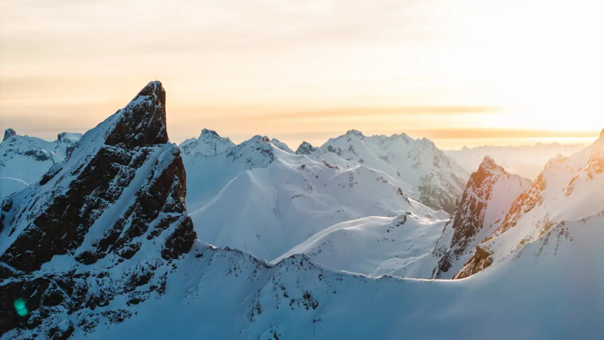 Verschneite Berggipfel mit untergehender Sonne im Hintergrund.