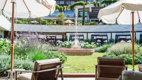 Chairs and parasols in front of a fountain on a terrace.