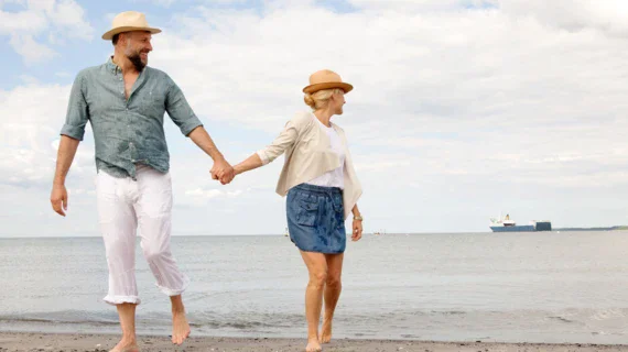 A. man and woman walking hand in hand along a beach with the sea in the background. 