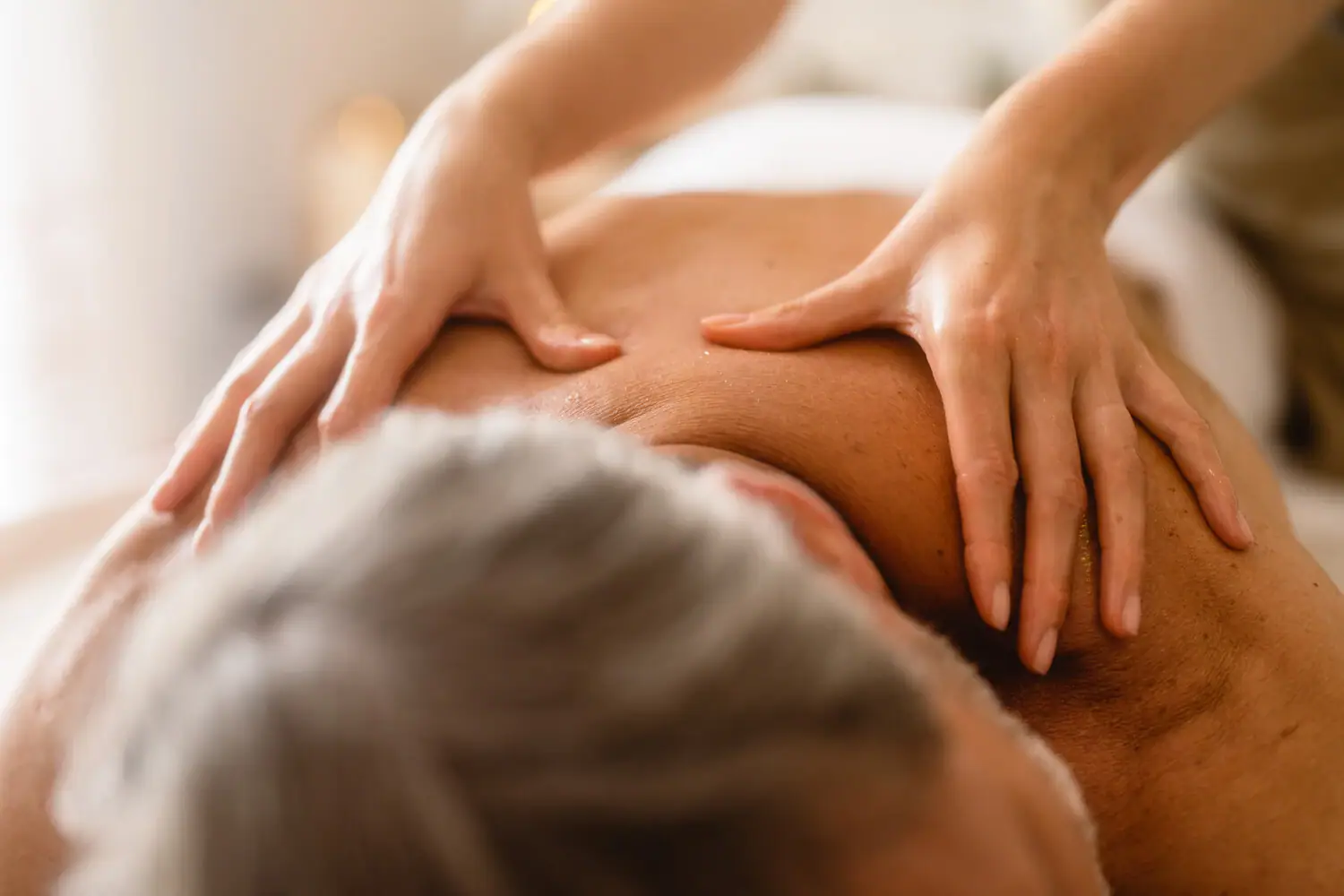 A person massaging a man's back indoors.
