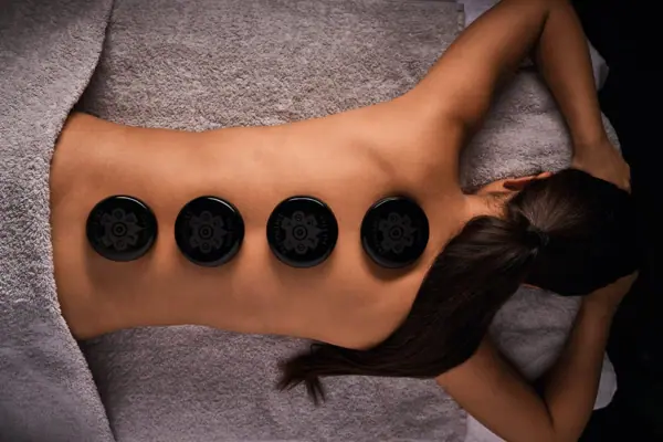 A woman lies on a towel with several black stones on her back.