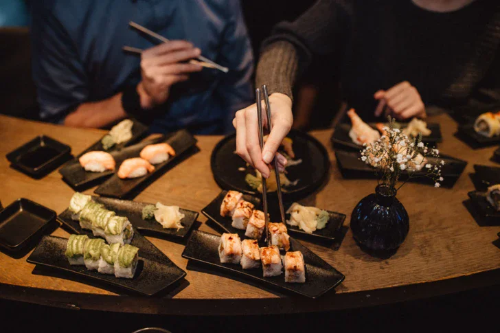 Multiple different sushi plates in a v shape on a wooden table with people sitting around. 