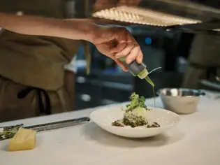 A chef pours green dressing onto a plate of food.