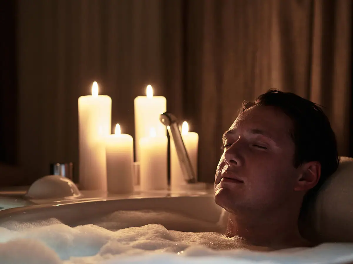A man relaxing in a bathtub surrounded by lit candles.