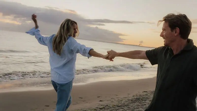 A man and woman holding hands on a beach.