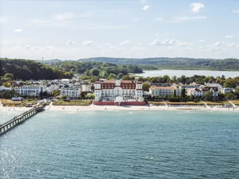 Large white building on the coast with beach and sea in the foreground.