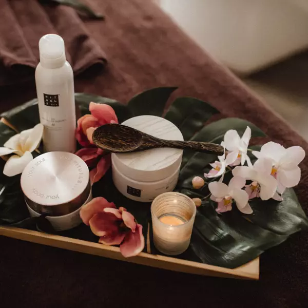 A wooden board with different Rituals products and flowers is placed on brown towels. 