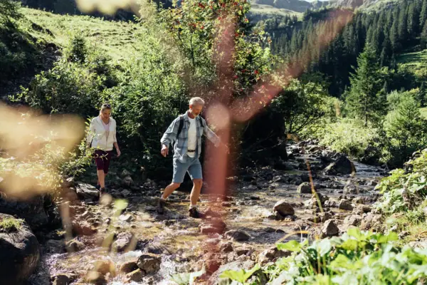 A man and a woman are balancing on stones in a stream.