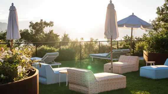 An outdoor lounging area with comfortable seating surround by greenery.