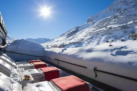 Snow-covered rooftop with chairs and tables, surrounded by snowy mountains.