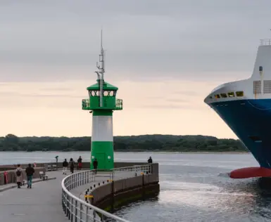 A pier with a green and white lighthouse next to a large ship.