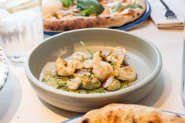 Kulinarik im A-RSOSA Gardasee Ein Teller mit Scampi hünsch angerichtet, auf einem Tisch mit anderen Speisen.