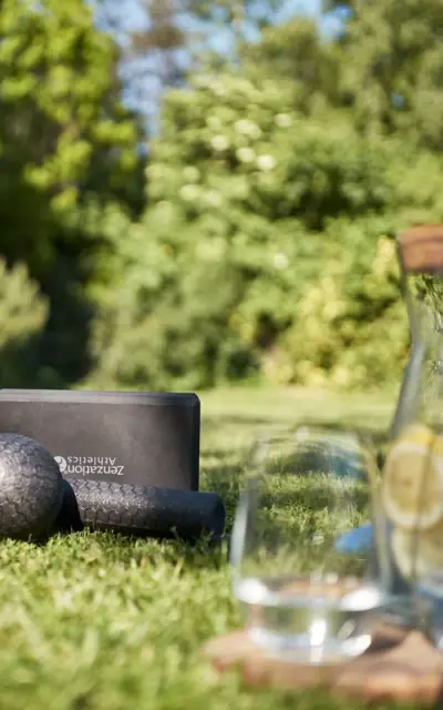 Yoga mats and a glass of water on grass with green trees in the background.