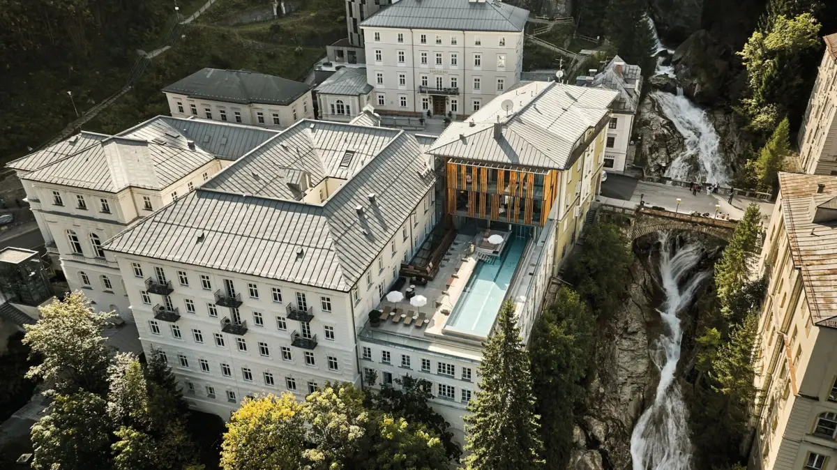 Straubinger Grand Hotel Aerial view of the Straubinger Grand Hotel in Bad Gastein, Austria, with Belle Époque architecture, outdoor pool and the iconic Bad Gastein waterfall in the Gastein Valley.